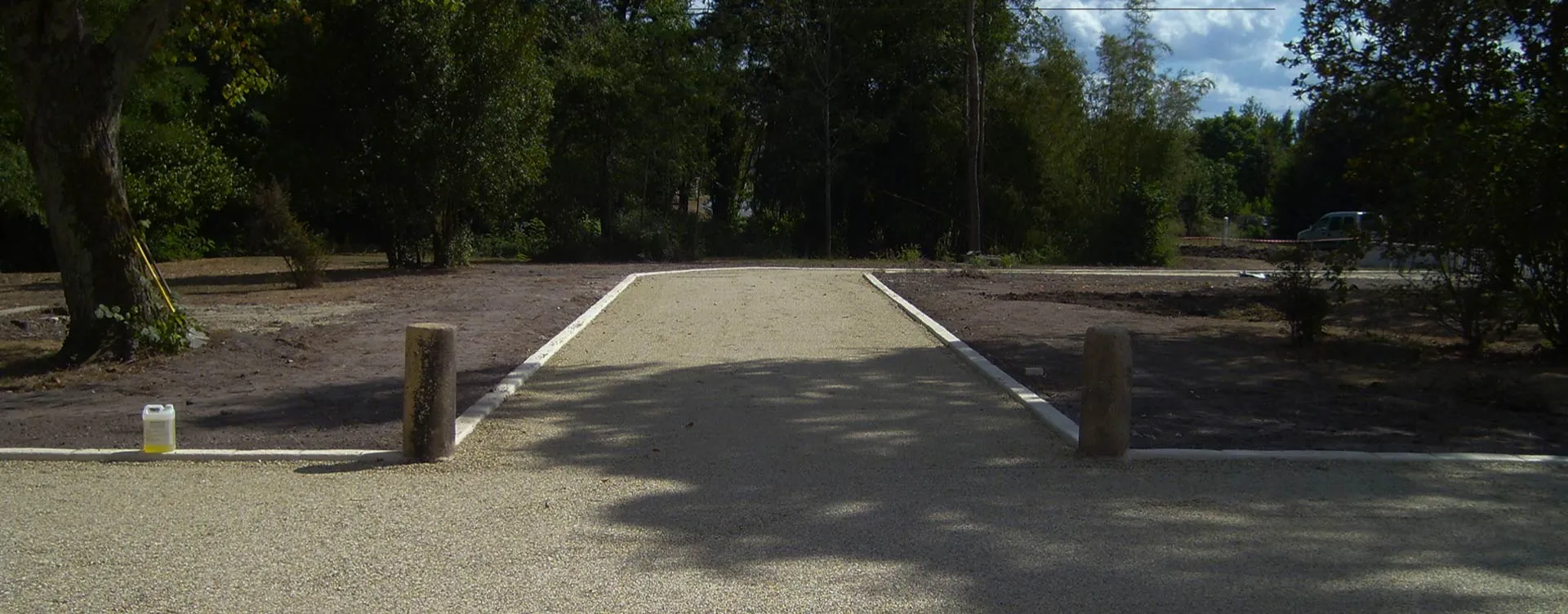 Allée en granulats clairs bordée de béton dans un espace arboré